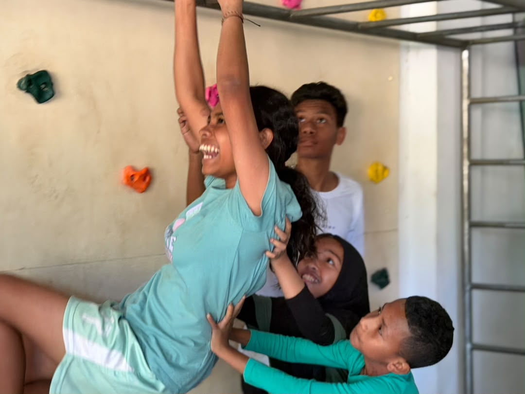 Students helping each other climb a colourful climbing wall